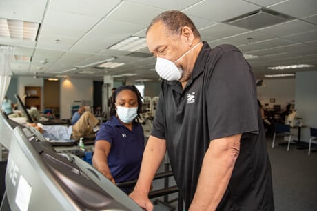 Older man wearing a cloth medical mask walking on a treadmill.