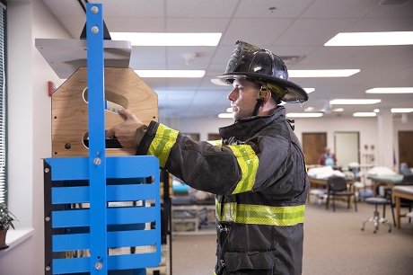 Male firefighter in full fire gear practicing safe lifting in a therapy gym